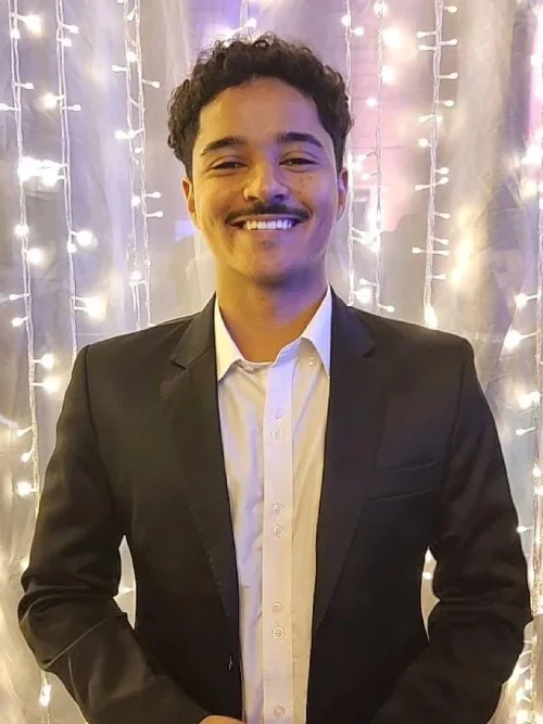 Fotografia profissional do Psicólogo Davi. Ele está usando um óculos de grau quadrado, traje social de terno e grafata, e está sorrindo.