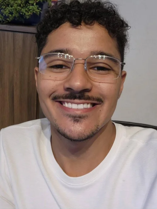 Fotografia profissional do Psicólogo Davi. Ele está usando um óculos de grau quadrado, camiseta branca e está sorrindo.